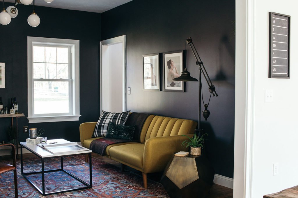 Yellow couhc in a black room with a white coffee table in front of it on a vintage rug.