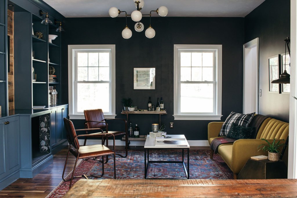 home library with black walls, a blue bookcase, a yellow couch, leather chairs, and a bar cart
