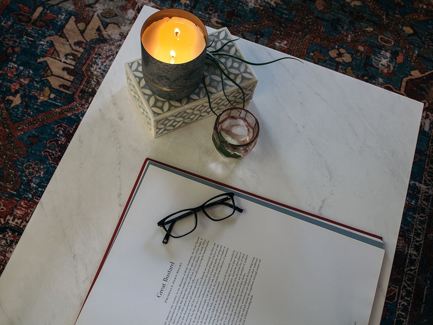 Marble coffee table on topof a vintage rug with a candle, book, and glasses.