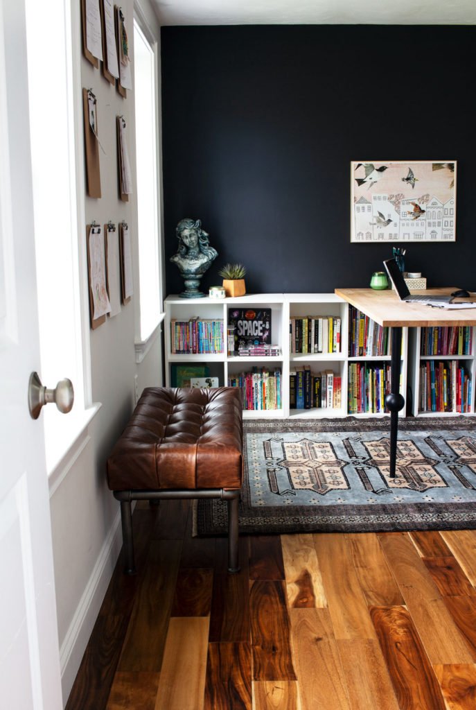 Looking through the doorway into a home office with a black accent wall, leather bench, and bookcase on that back wall.