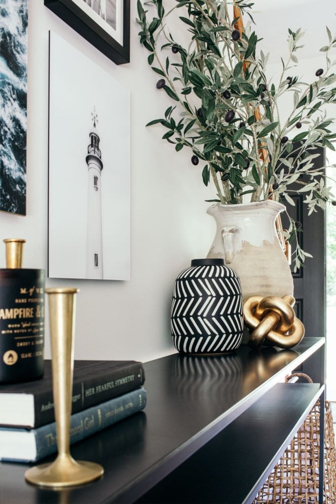 styled entryway with narrow console table, brass candlesticks, olive branches and coastal artwork