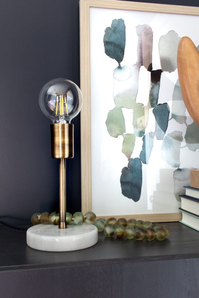 Marble and brass lamp on nightstand in dark bedroom in front of abstract art