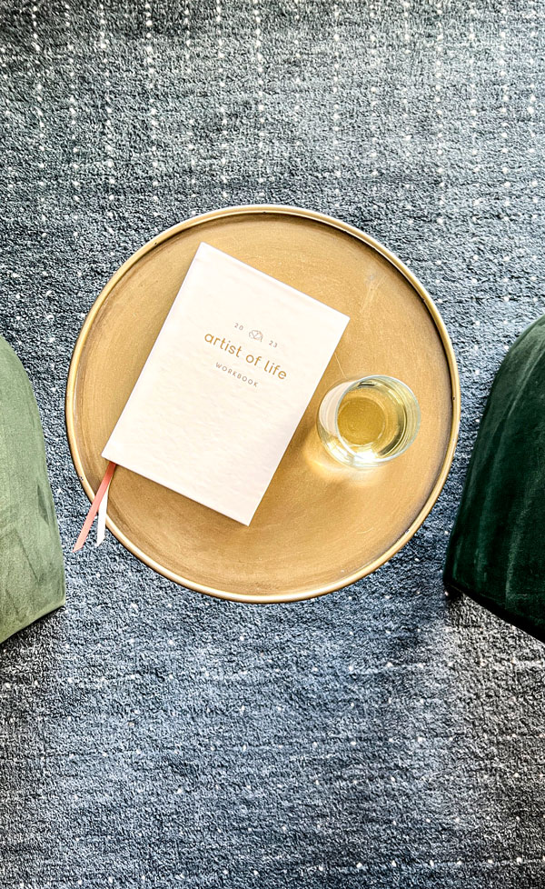 Glass of white wine and a 2023 white leather journal laying on top of an antique brass drink table.