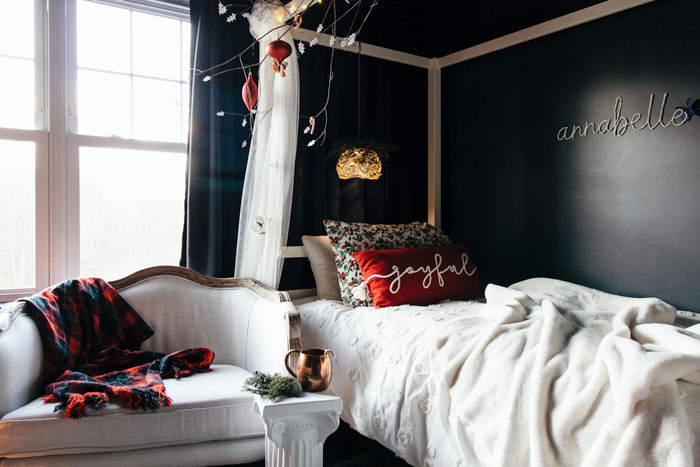 Red Christmas pillow with plaid on couch, decorating a white canopy bed.