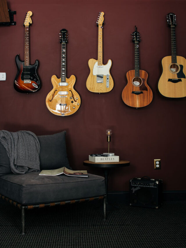 Guitars hanging on a dark red wall. Slate blue chair in foreground with amp.