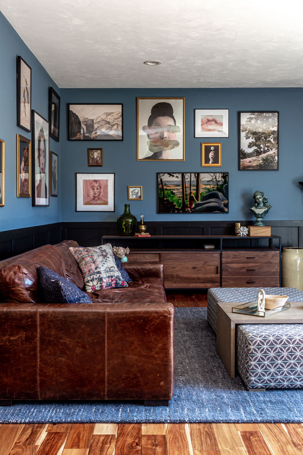 Blue and black living room with large salon gallery wall, wainscoting, corner fireplace and leather couch.