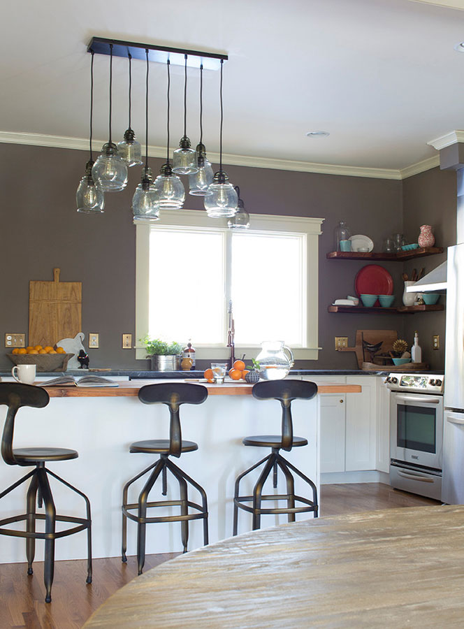 Industrial metal counter stools at butcher block kitchen island with white cabinets and soapstone counters