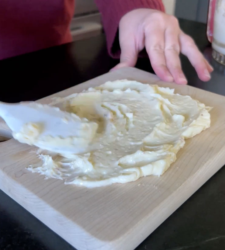 Spread butter artfully onto a wooden board using a loose swirling motion