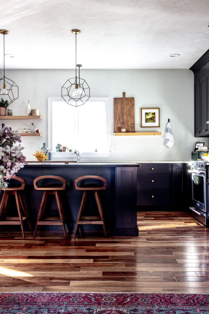 Black kitchen with with walls and a black island with soapstone countertop and walnut counter stools. White britannica quartz counters in the background