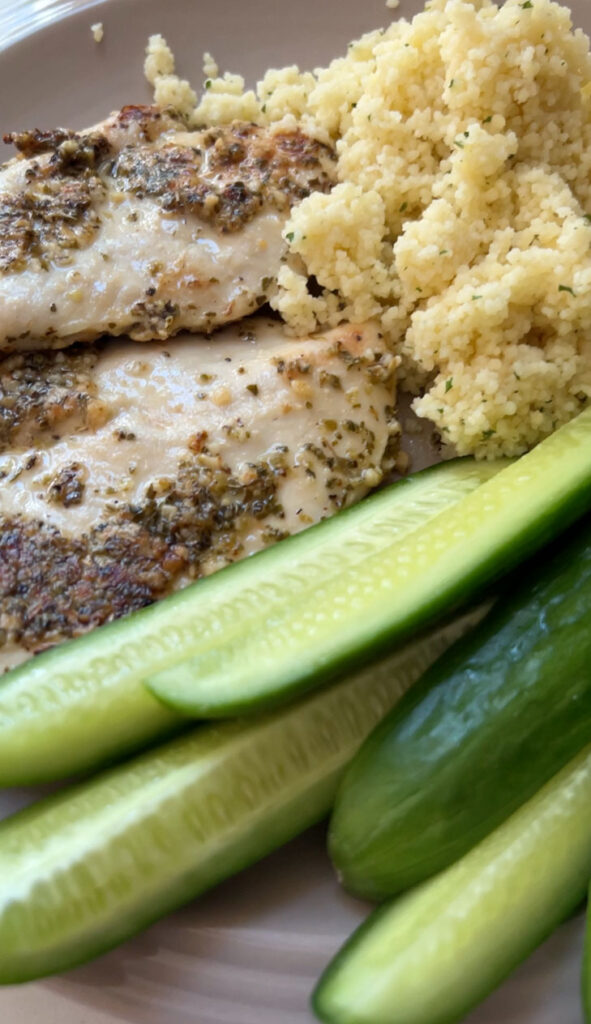 Lemon oregano chicken with cous cous and cucumbers on a plate.