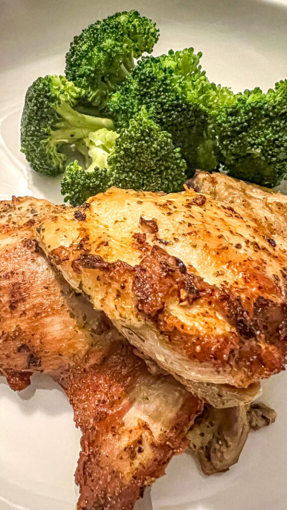 Lemon garlic chicken thighs on a white plate with crisp steamed broccoli.