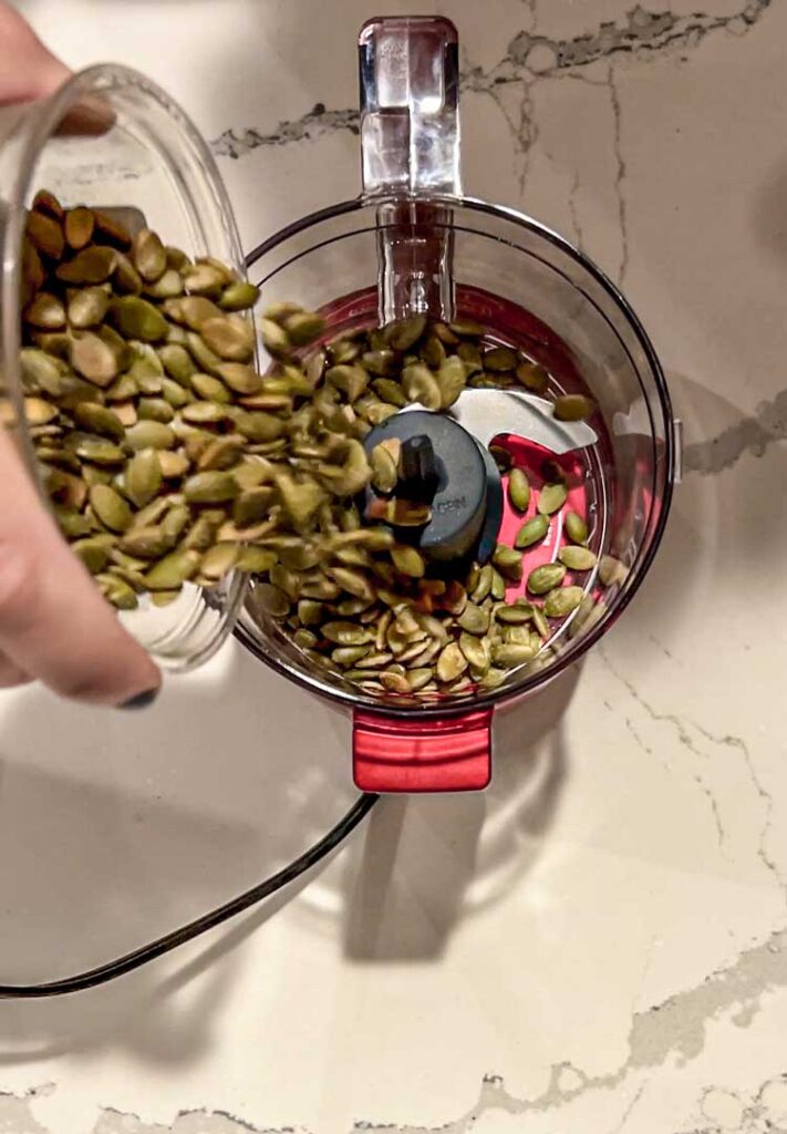 Hand pouring pepitas into a mini food processor