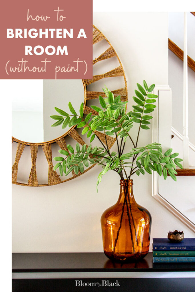 Large rattan mirror over a black console table with an orange vase with acacia branches on top.
