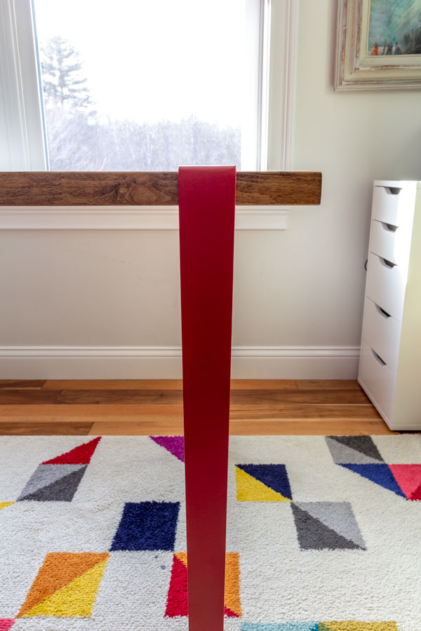 Close-up of a red metal leg attached to a slab of butcher block.