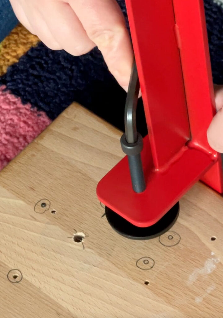 Hands attaching a red metal leg to a piece of butcher block.