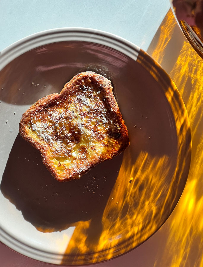 Croissant french toast on a tan plate in a ray of sunshine.