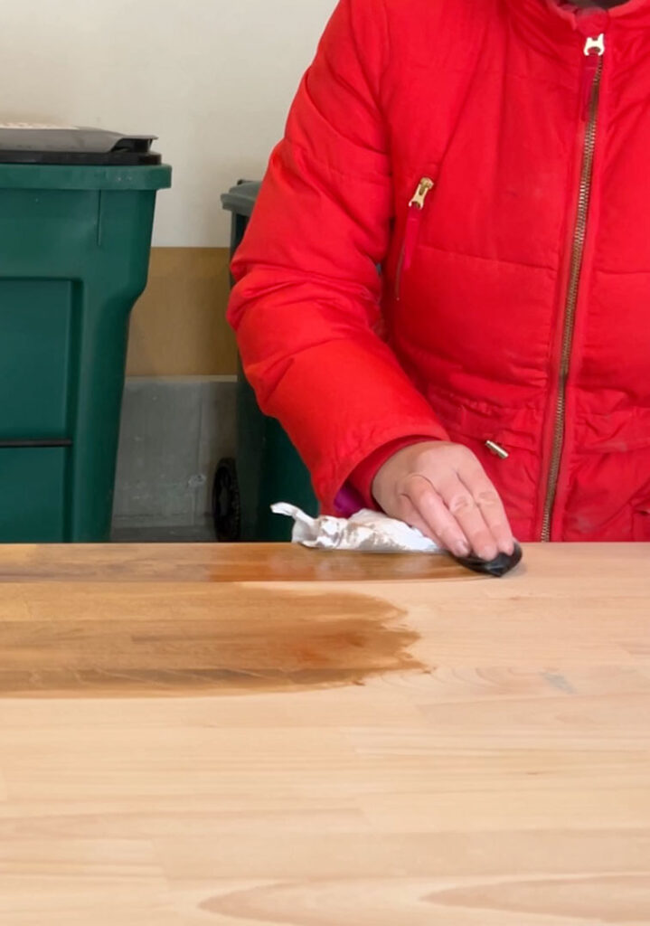 Woman in a red coat applying stain to wood.