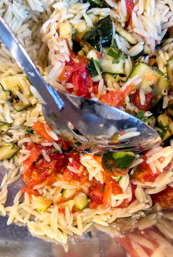 Spoon mixing a large bowl of grilled zucchini pasta salad.