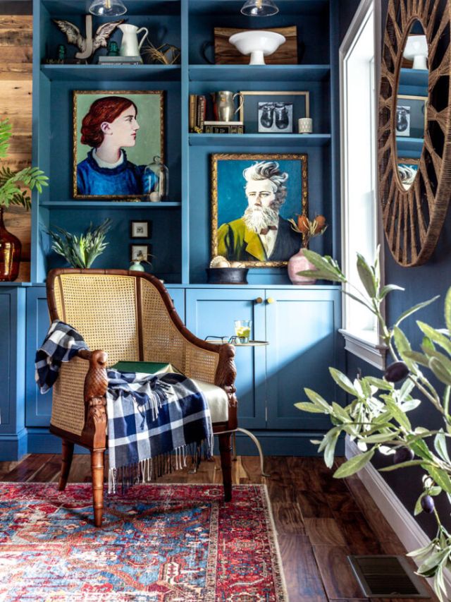 Cane chair in front of a blue built-in bookcase styled with large paintings and vintage decor. 