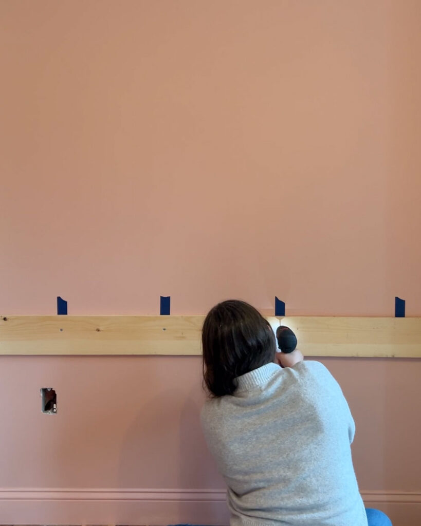 Woman screwing a piece of wood into the wall.