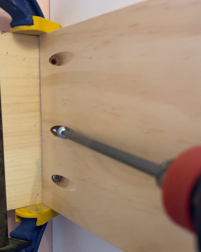 Clamp holding two boards while a pocket screw is being drilled.