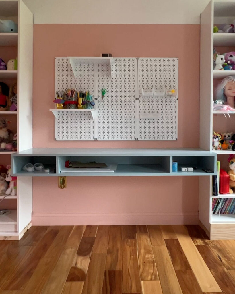 Blue floating desk on a pink wall flanked by white bookcases.
