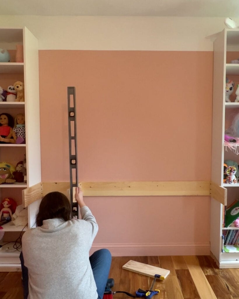 Woman holding a level against a floating desk to make sure everything is straight.