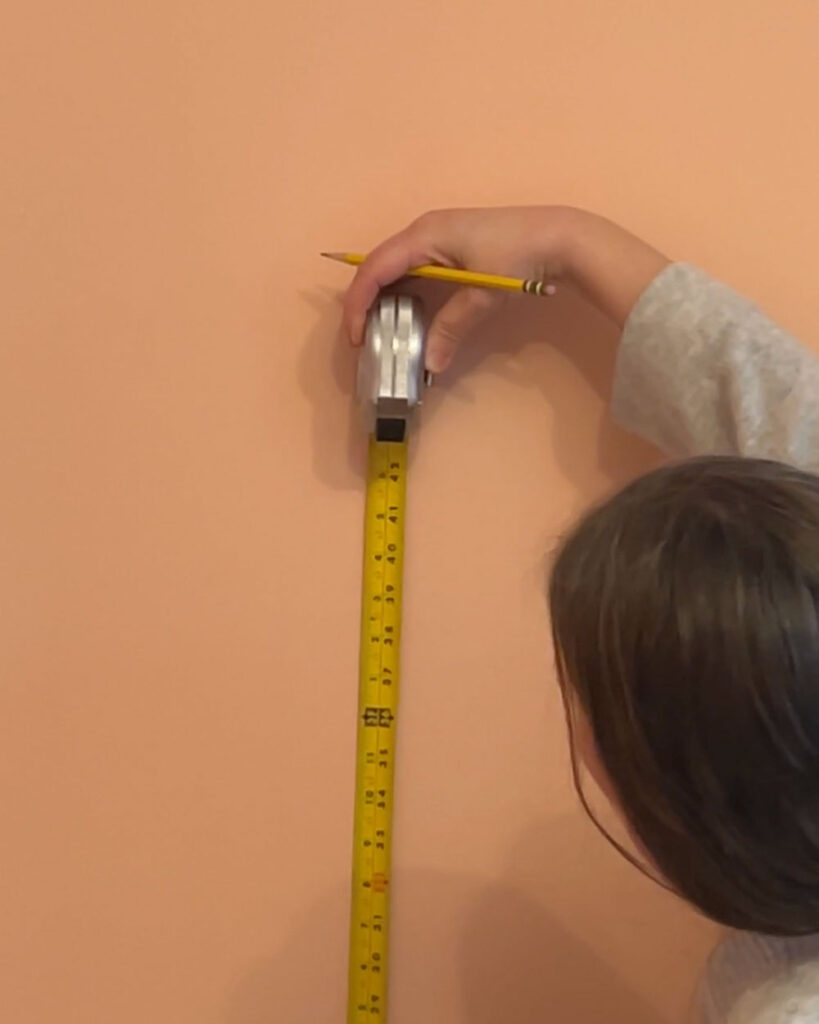 Woman holding a measuring tape against a pink wall.