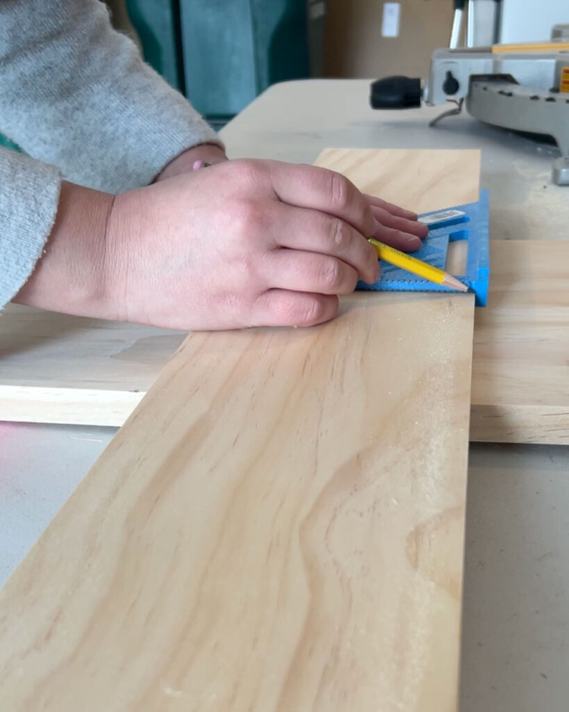 Close-up of hands marking a measurement on a board using a speed square.