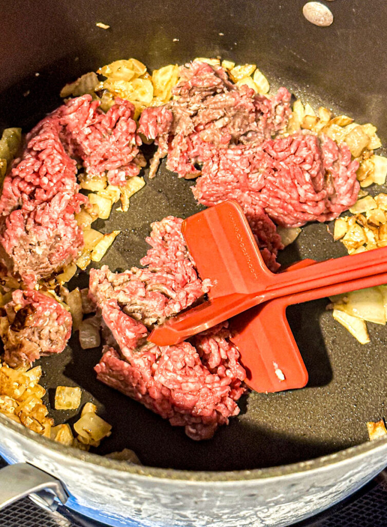 Ground beef and onion being cooked in a pot being mixed with a Chop Stir.
