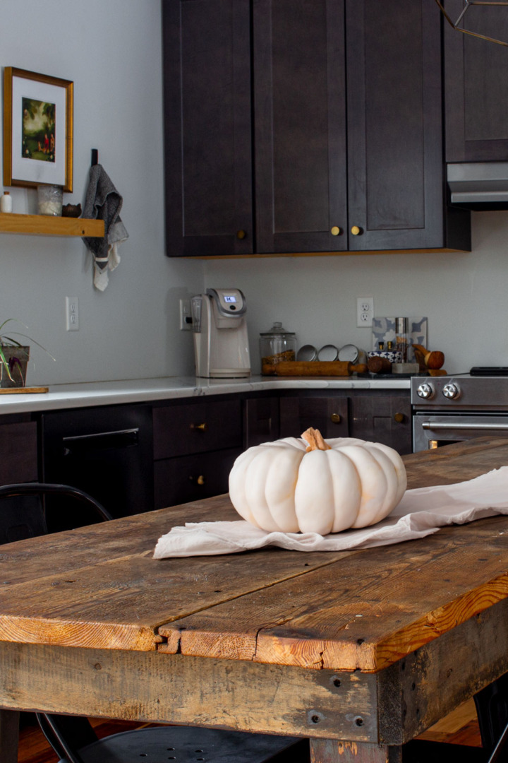 Reclaimed wood table in a dark kitchen with a pumpkin on top.