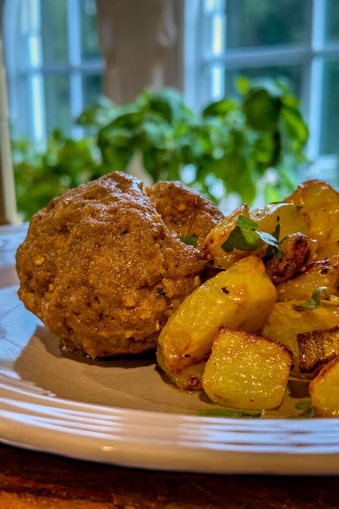 Close-up of meatloaf and roasted potatoes on a plate in front of a window.