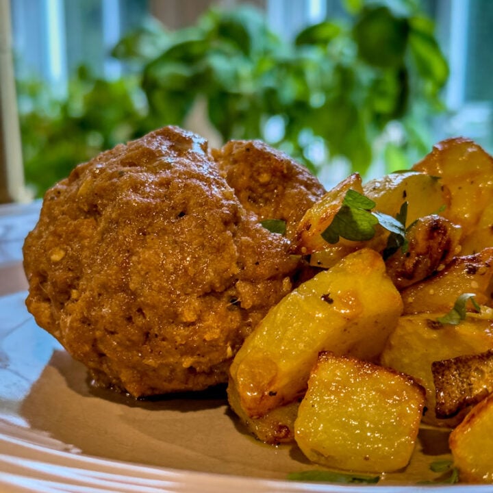 Close-up of meatloaf and roasted potatoes on a plate in front of a window.