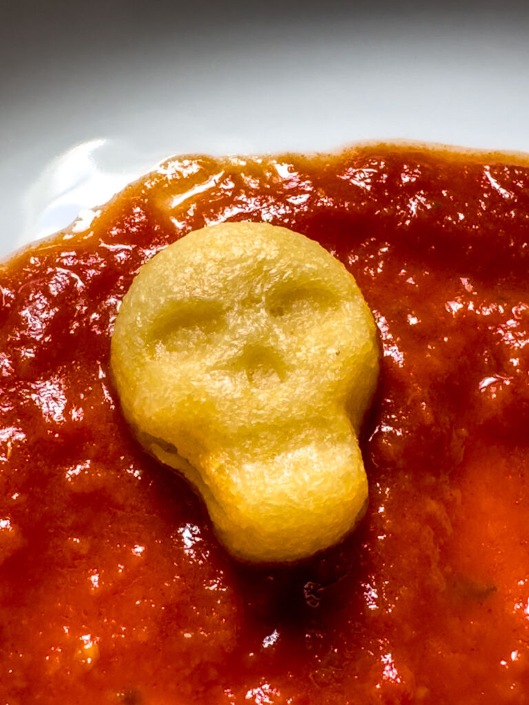 Skull shaped polenta in marinara sauce in a white bowl.