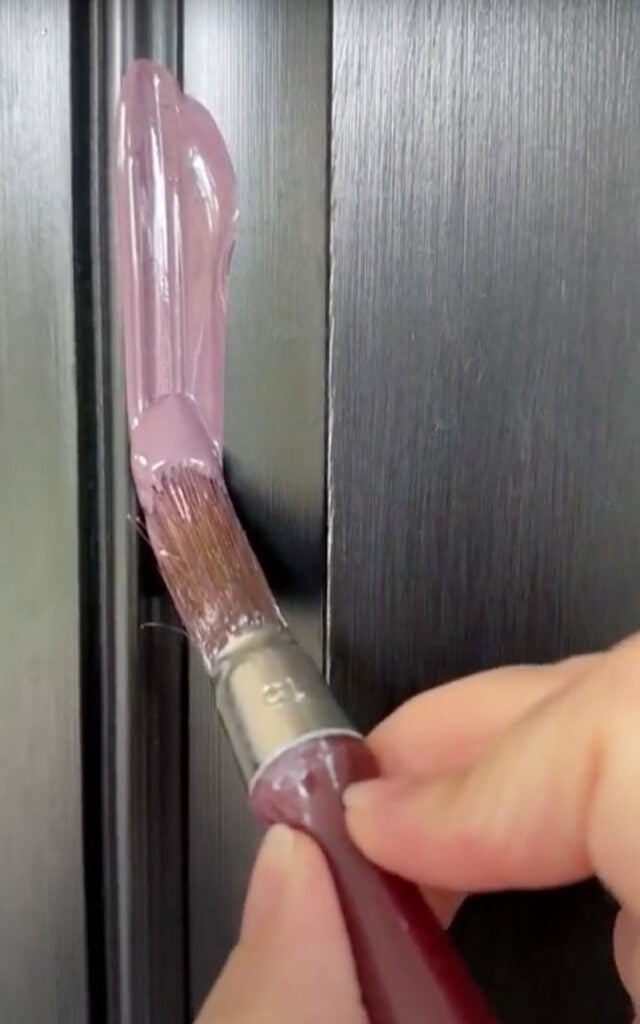 Close-up of a hand using a trim brush to paint a black front door purple.