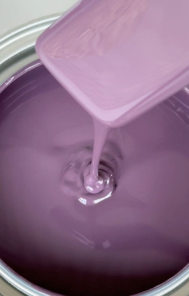 Close-up of purple paint dripping from a stir stick into a can of paint.