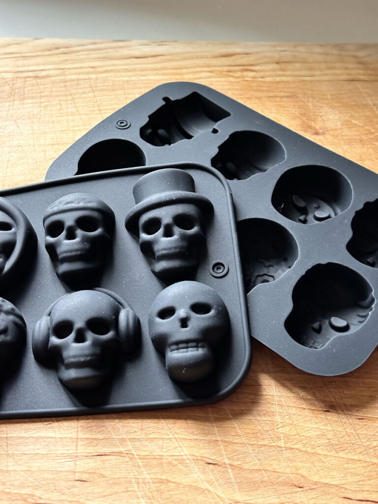 Two black silicone skull molds sitting on a cutting board.