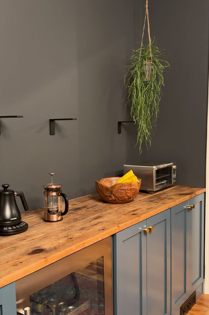Black brackets attached to a black wall above a blue breakfast bar with a reclaimed wood counter.