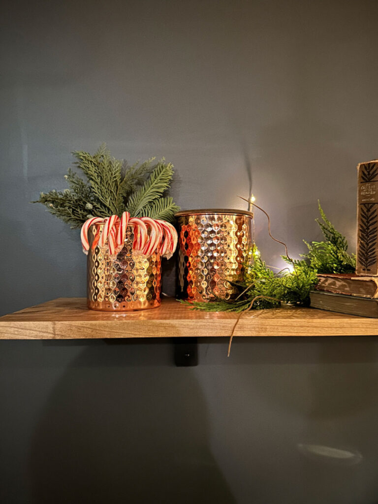 Copper canisters with candy canes on a shelf decorated for Christmas.