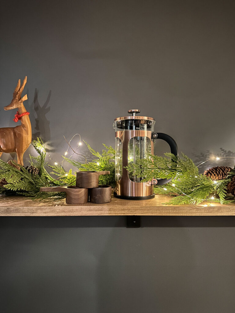 Copper french press with wooden scoops on a shelf decorated for Christmas.