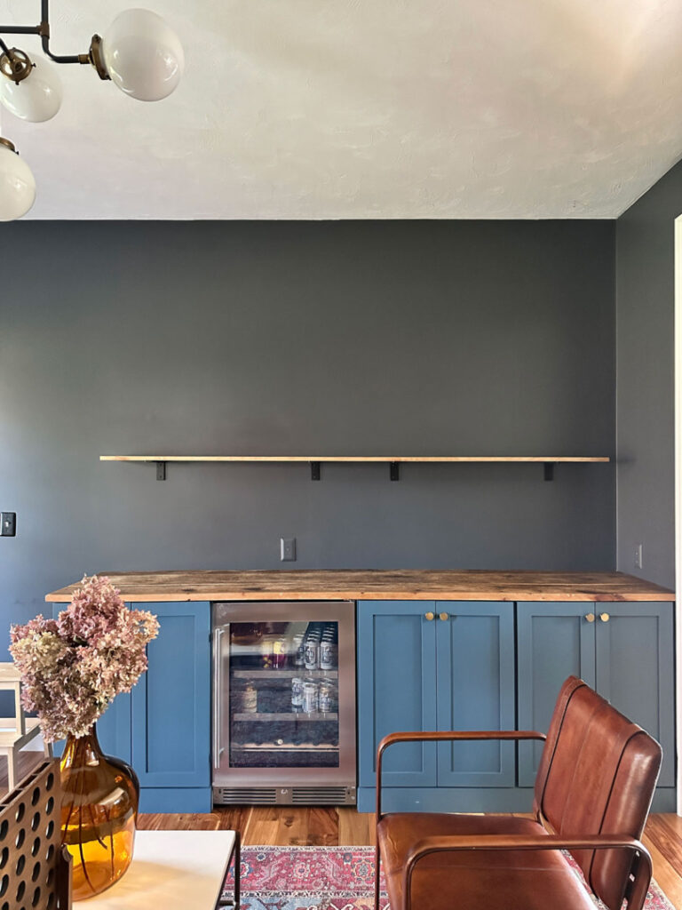 Long shelf on a black wall above a blue breakfast bar.