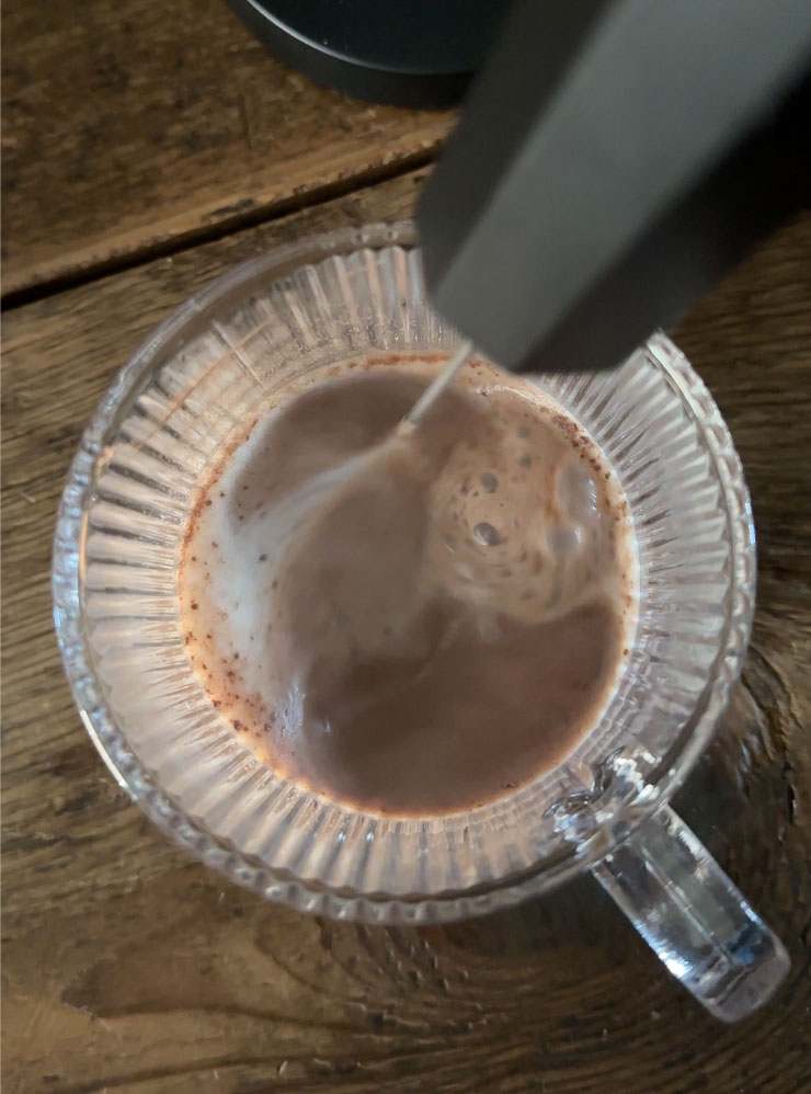 Mini electric whisker mixing hot cocoa in a glass mug.